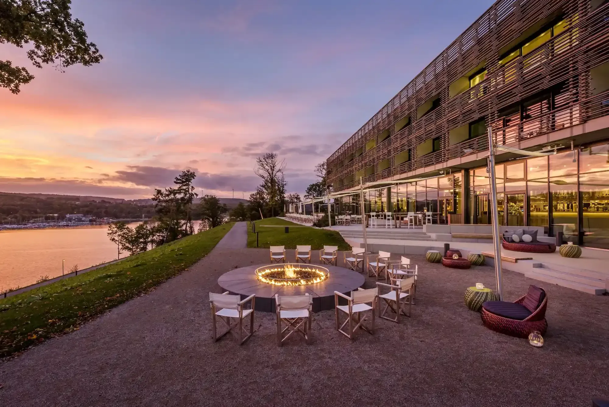 Feuerstelle mit Stühlen vor der Seezeitlodge in der Abenddämmerung, im Hintergrund der Bostalsee – Yoga Hotel in Deutschland