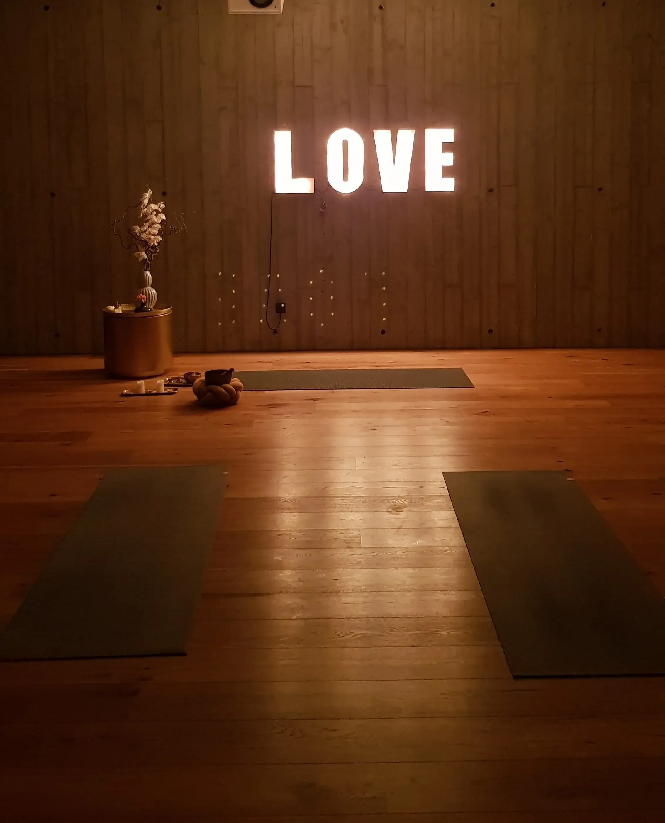 Abendlich beleuchteter Yogaraum mit Holzboden, Yogamatten, Klangschale und LOVE-Leuchtschrift – Yogaraum im Hotel Das Kubatzki an der Nordsee